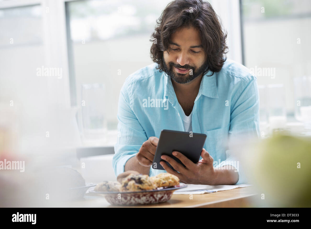 Una oficina o un apartamento interior en la Ciudad de Nueva York un hombre barbado en una camiseta de color turquesa con una tableta digital Foto de stock