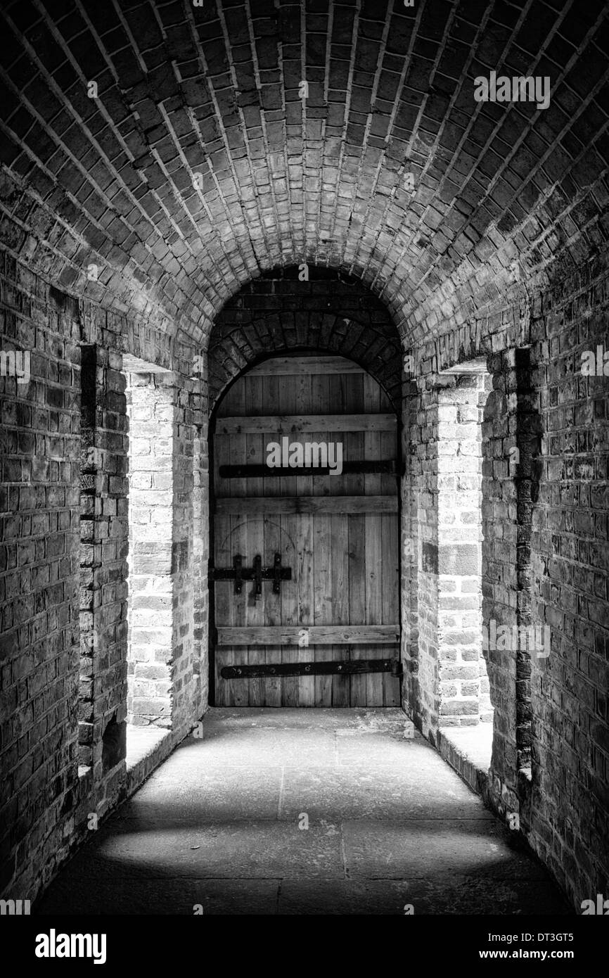 Revestidos de ladrillo de túnel que conduce a una antigua puerta de madera en una fortaleza de la época de la Guerra Civil. Convertir a blanco y negro. Foto de stock