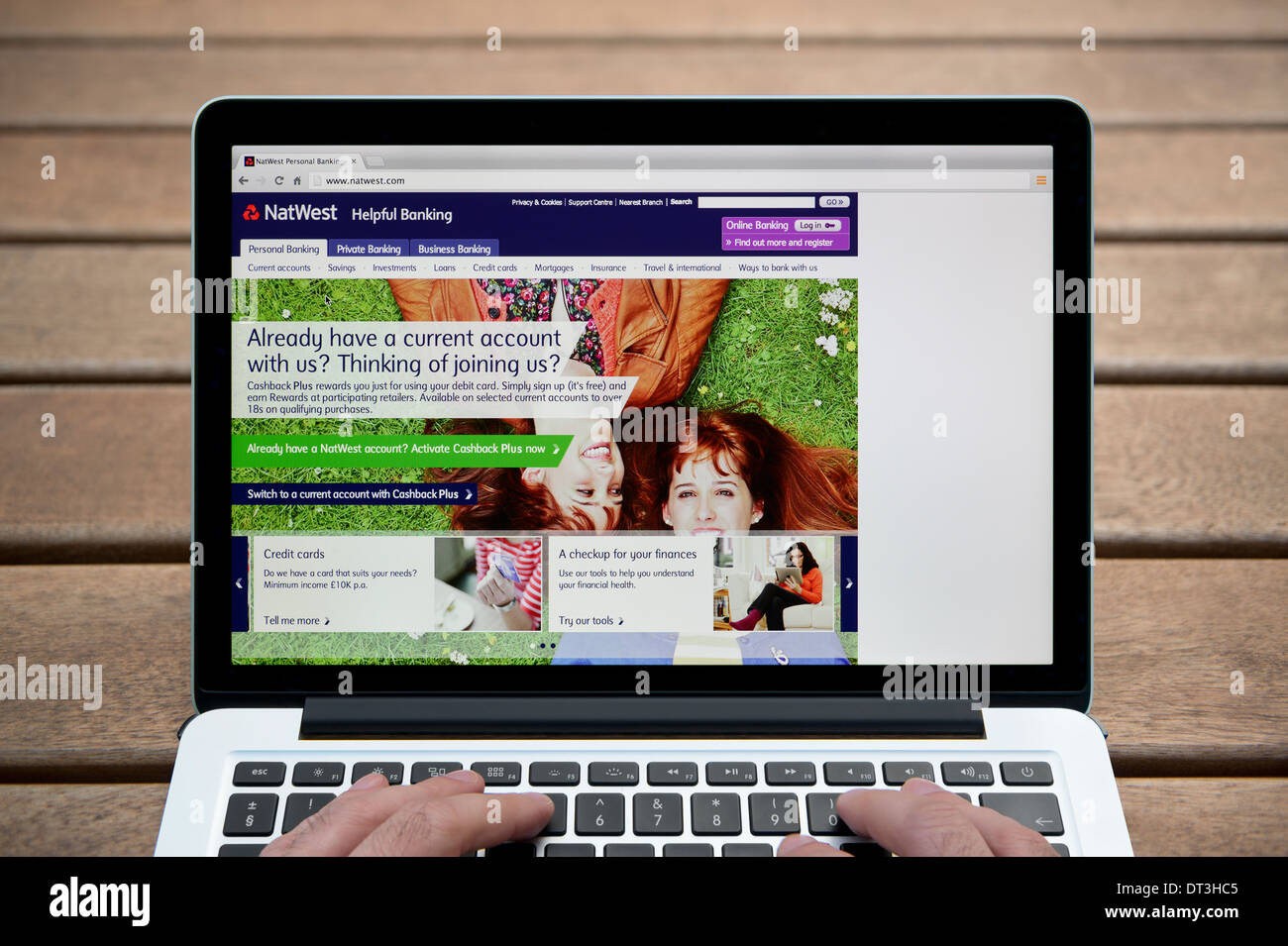 El Natwest web sobre un MacBook contra un banco de madera de fondo al aire libre incluyendo un hombre de dedos (uso Editorial solamente). Foto de stock