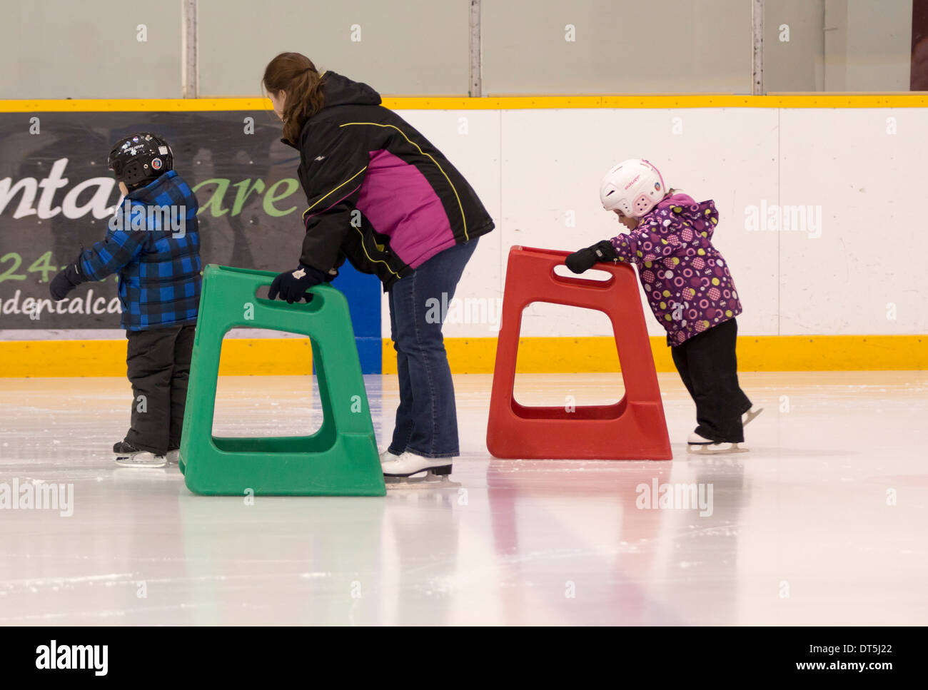 Madre, hijo e hija aprender patinar en el hielo con la asistencia en pista de patinaje cubierta Foto de stock