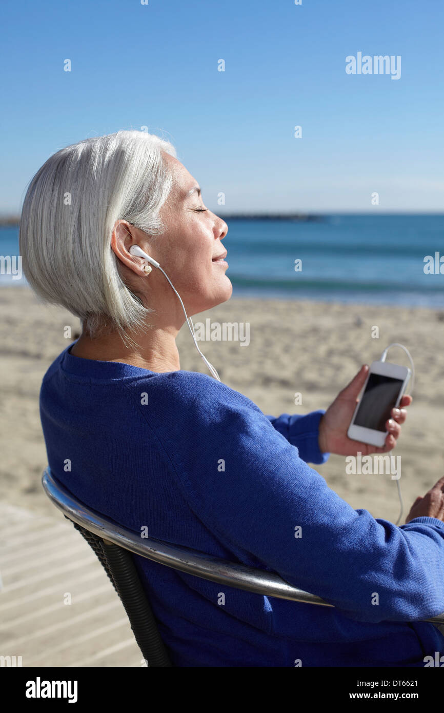 Mujer madura, escuchar música con auriculares en la playa Foto de stock