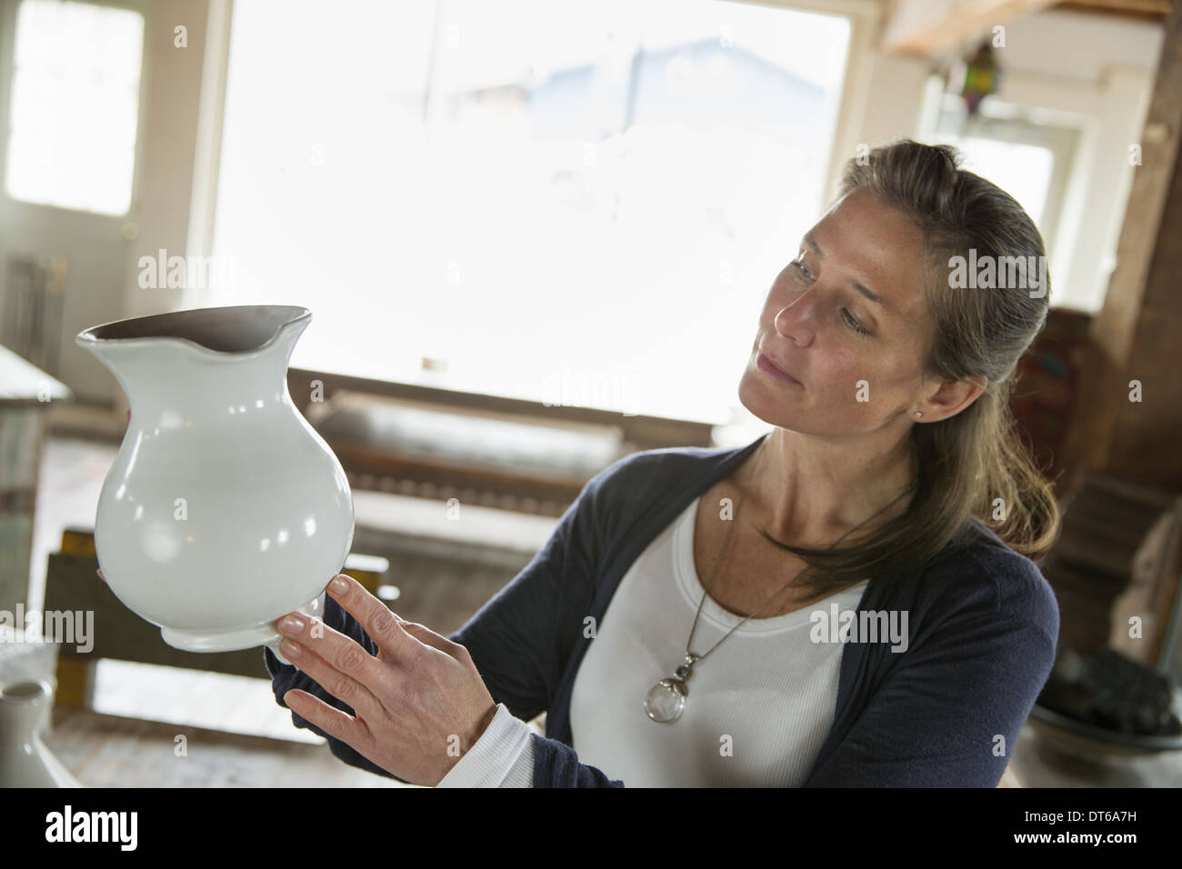 Una mujer que sostiene una jarra de cerámica blanca en un antiguo almacén de muebles y mercancías. Foto de stock
