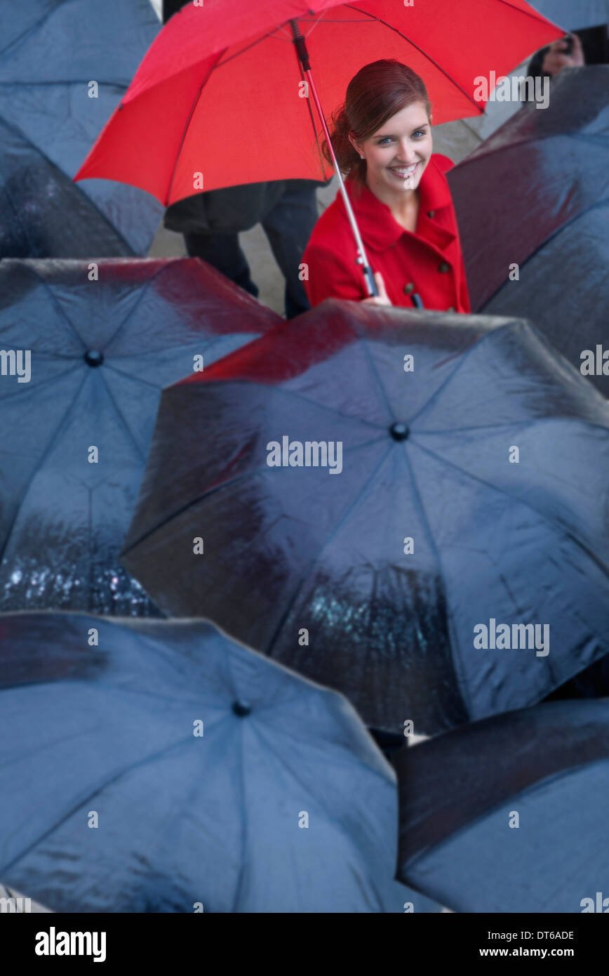 Mujer joven con sombrilla roja entre los Paraguas negro Foto de stock