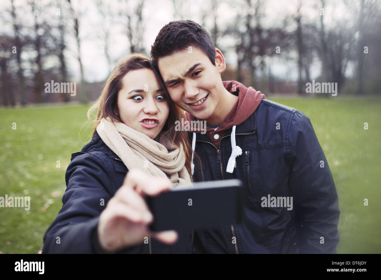 La pareja de adolescentes divertido fotografiar a sí mismos con smart phone en el parque. Linda chica con su novio tomando fotos. Foto de stock