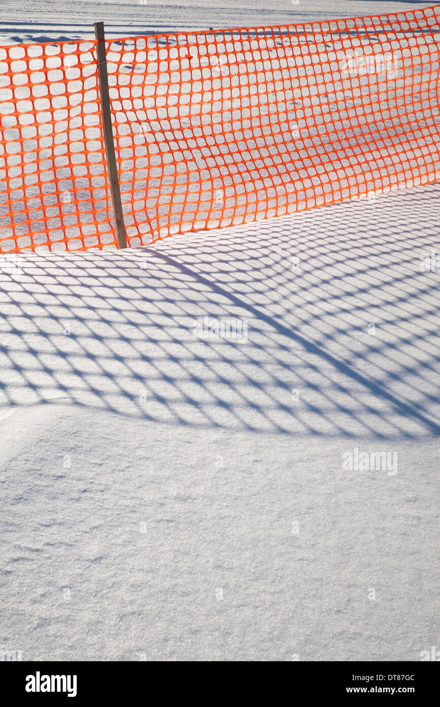 Las sombras de un cerco de nieve de plástico naranja hacer patrones en la nieve de Nueva Inglaterra. Foto de stock