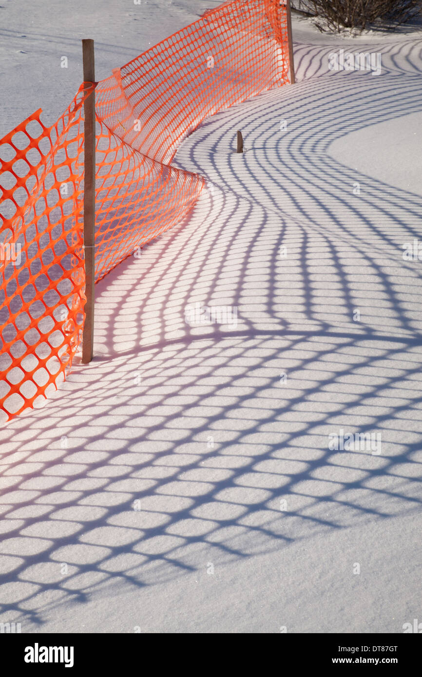 Las sombras de un cerco de nieve de plástico naranja hacer patrones en la nieve de Nueva Inglaterra. Foto de stock