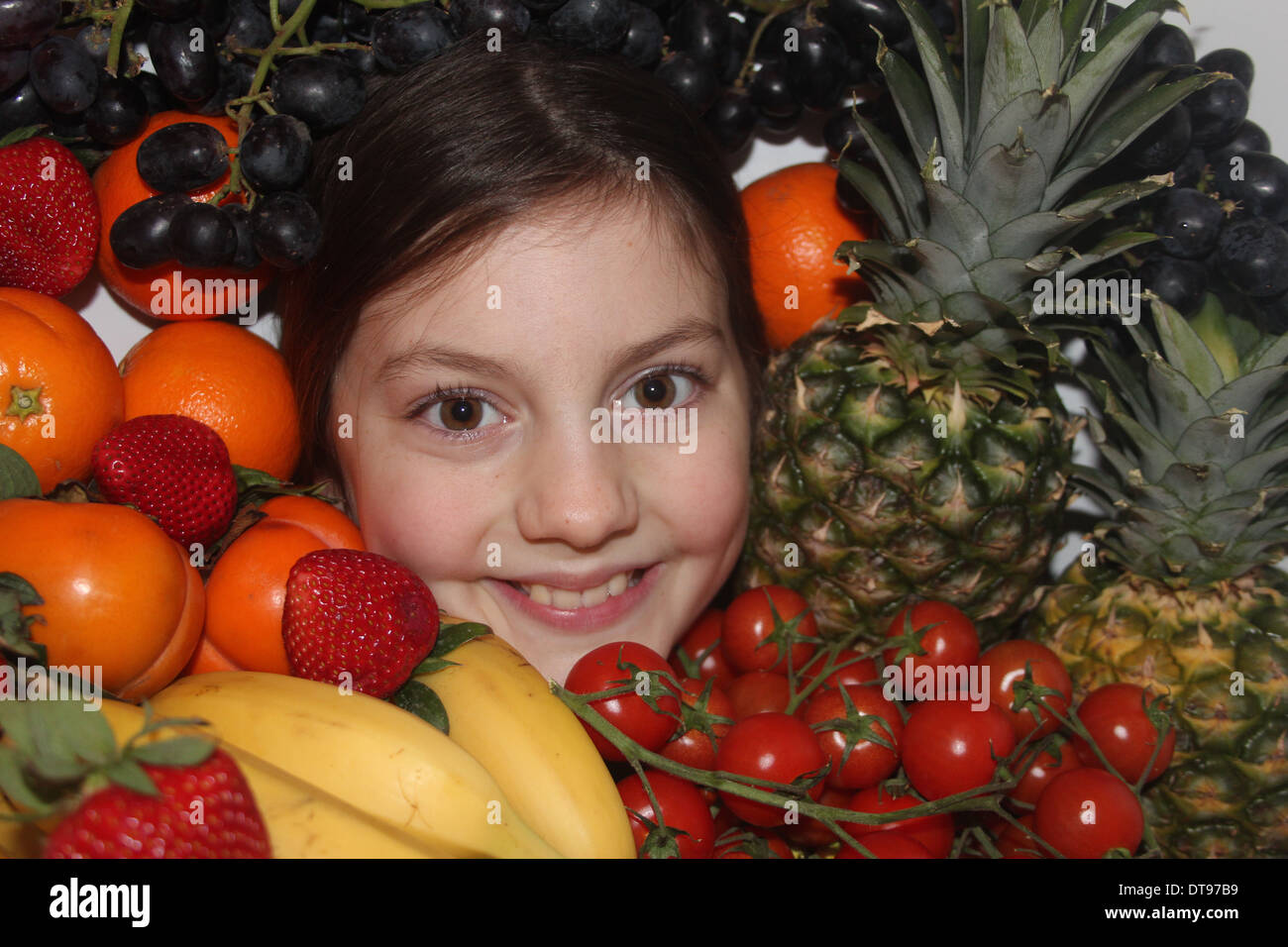 Los jóvenes caucásicos cara de la niña rodeada de frutales y hortalizas, cinco al día, Inglaterra, Reino Unido. Foto de stock