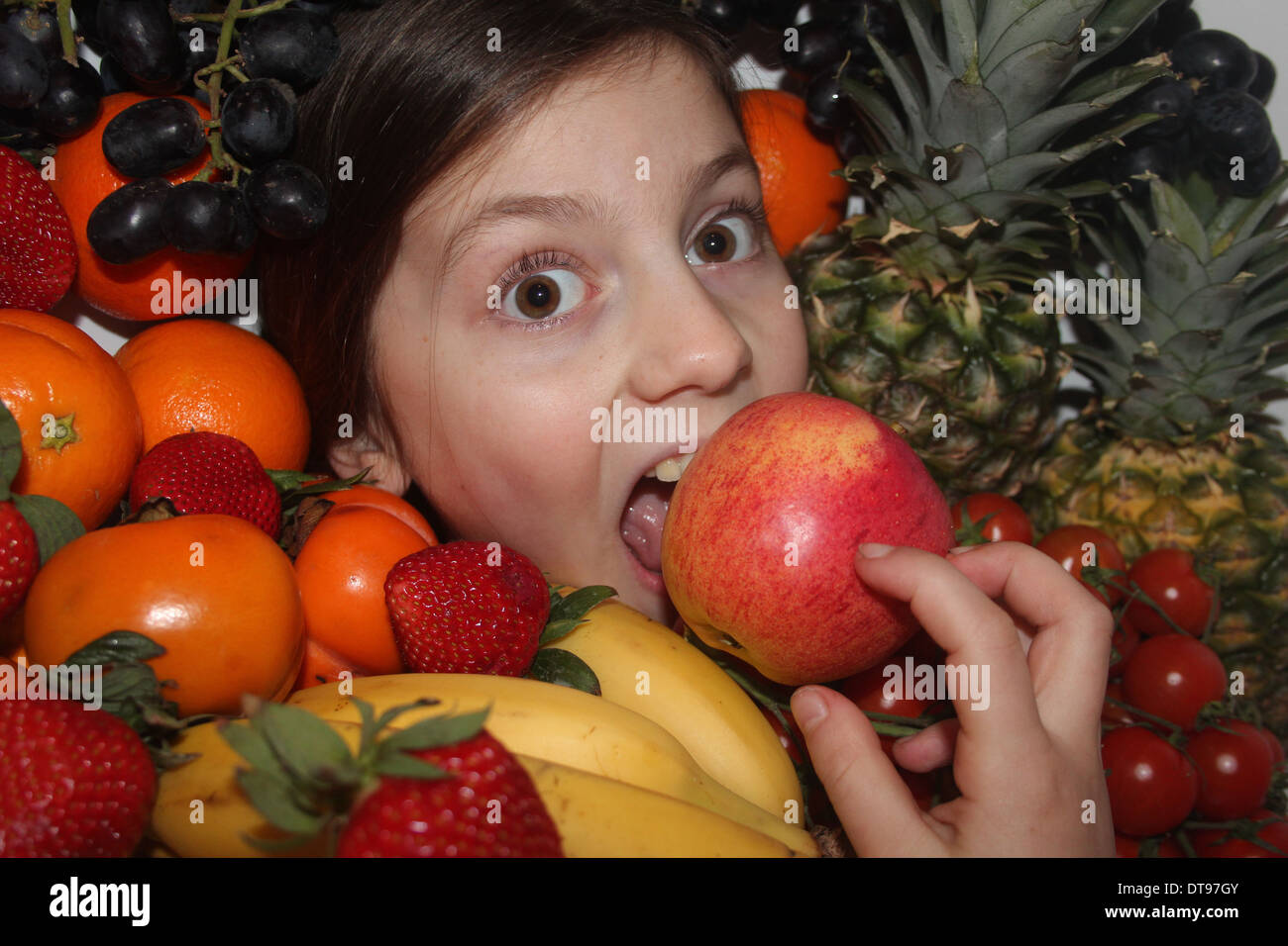Los jóvenes caucásicos cara de la niña rodeada de frutales y hortalizas, comiendo una manzana, cinco al día, Inglaterra, Reino Unido. Foto de stock