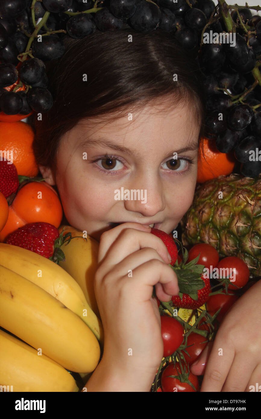 Los jóvenes caucásicos cara de la niña rodeada de frutales y hortalizas comiendo una fresa, cinco al día, Inglaterra, Reino Unido. Foto de stock