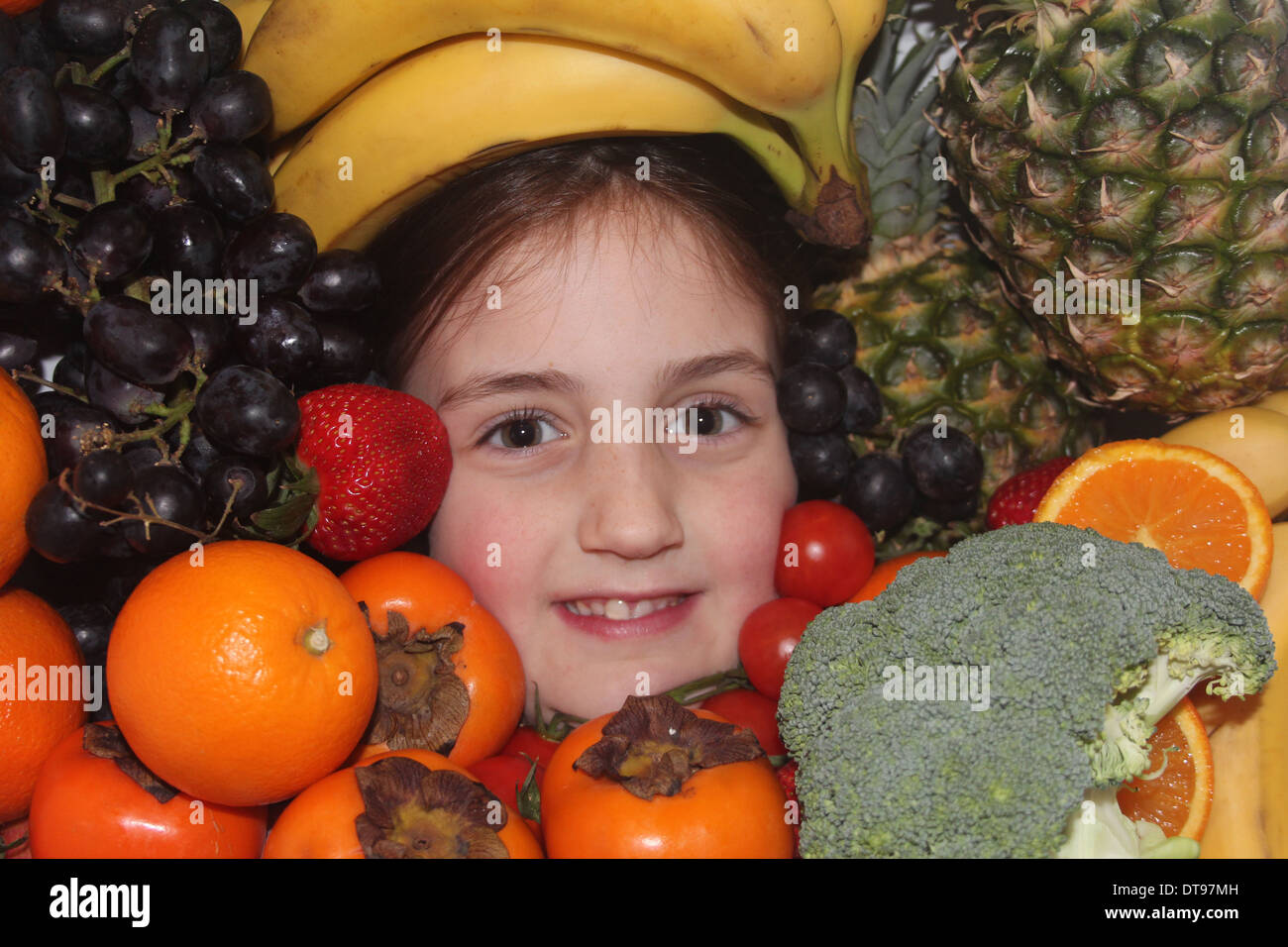 Los jóvenes caucásicos cara de la niña rodeada de frutales y hortalizas, cinco al día, Inglaterra, Reino Unido. Foto de stock