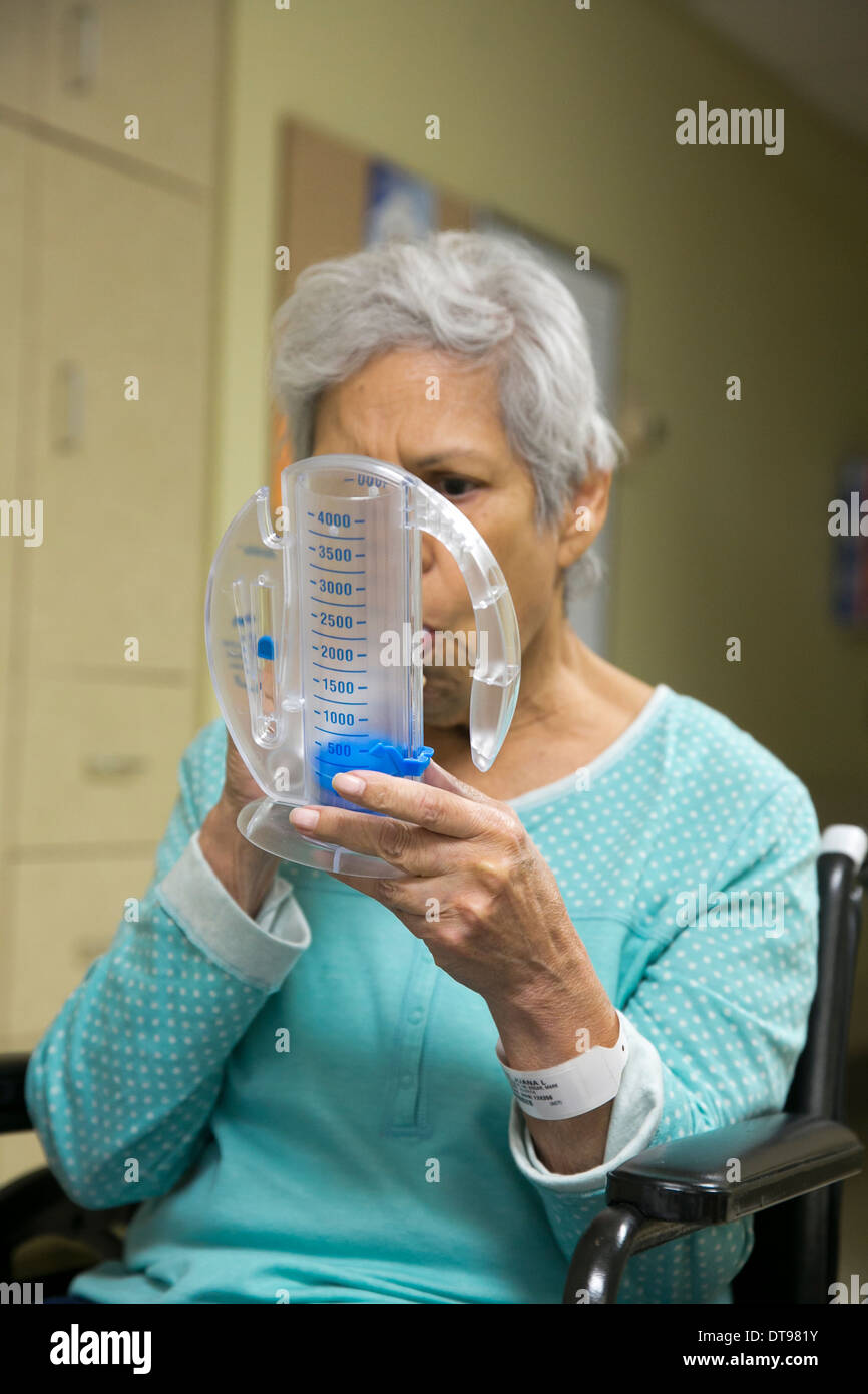 Hispano de 75 años senior citizen utiliza un aparato de ejercicios respiratorios médicos mientras que en un hospital de rehabilitación en Texas. Foto de stock