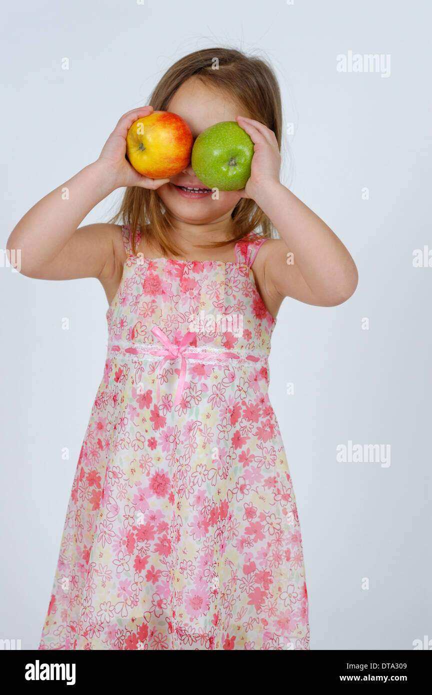 Chica con una manzana roja y verde en la parte delantera de la cara Foto de stock