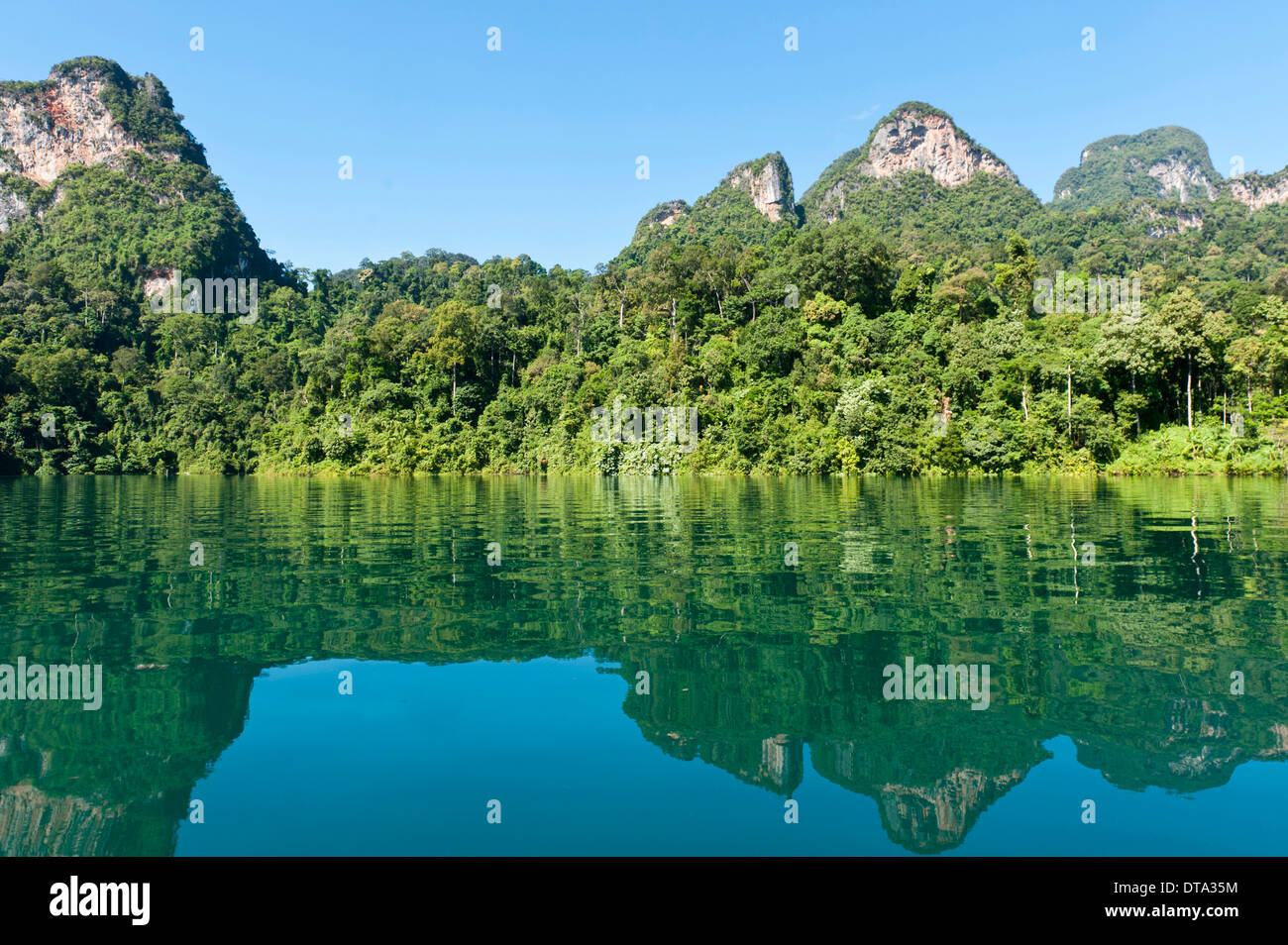 Karst boscosas montañas de piedra caliza con vegetación selvática que se refleja en el agua, depósito Rachabrapha, Chiao Lago Léman Foto de stock