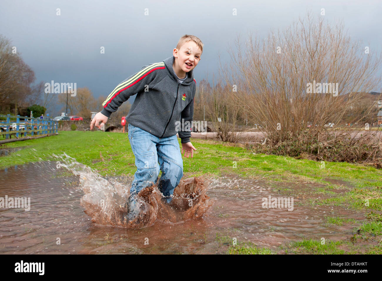 Un joven disfrutando el clima húmedo saltando en un charco y salpicaduras de agua. Foto de stock