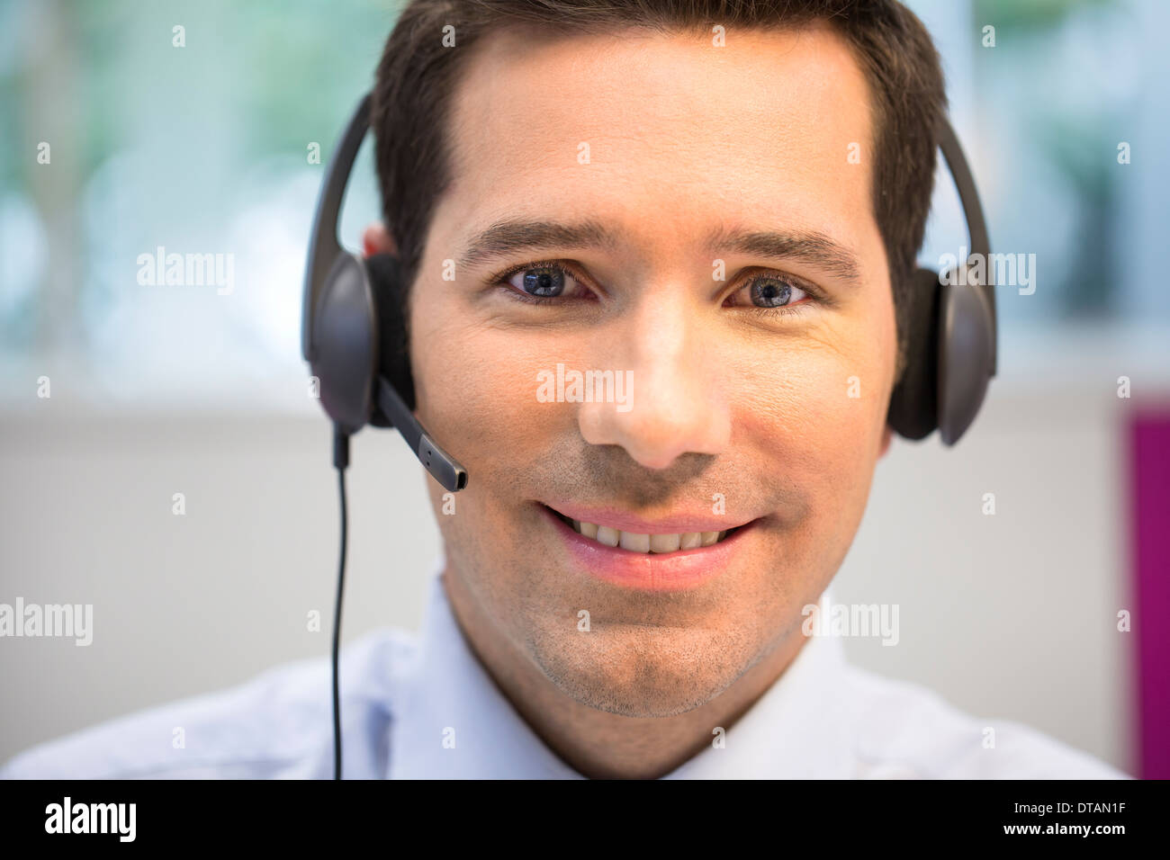 Retrato del empresario en la oficina por teléfono con auriculares, mirando la cámara Foto de stock