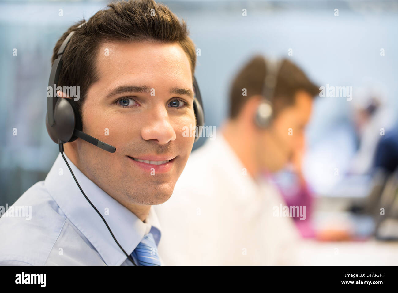 Retrato de operador en la oficina por teléfono con auriculares, mirando la cámara Foto de stock