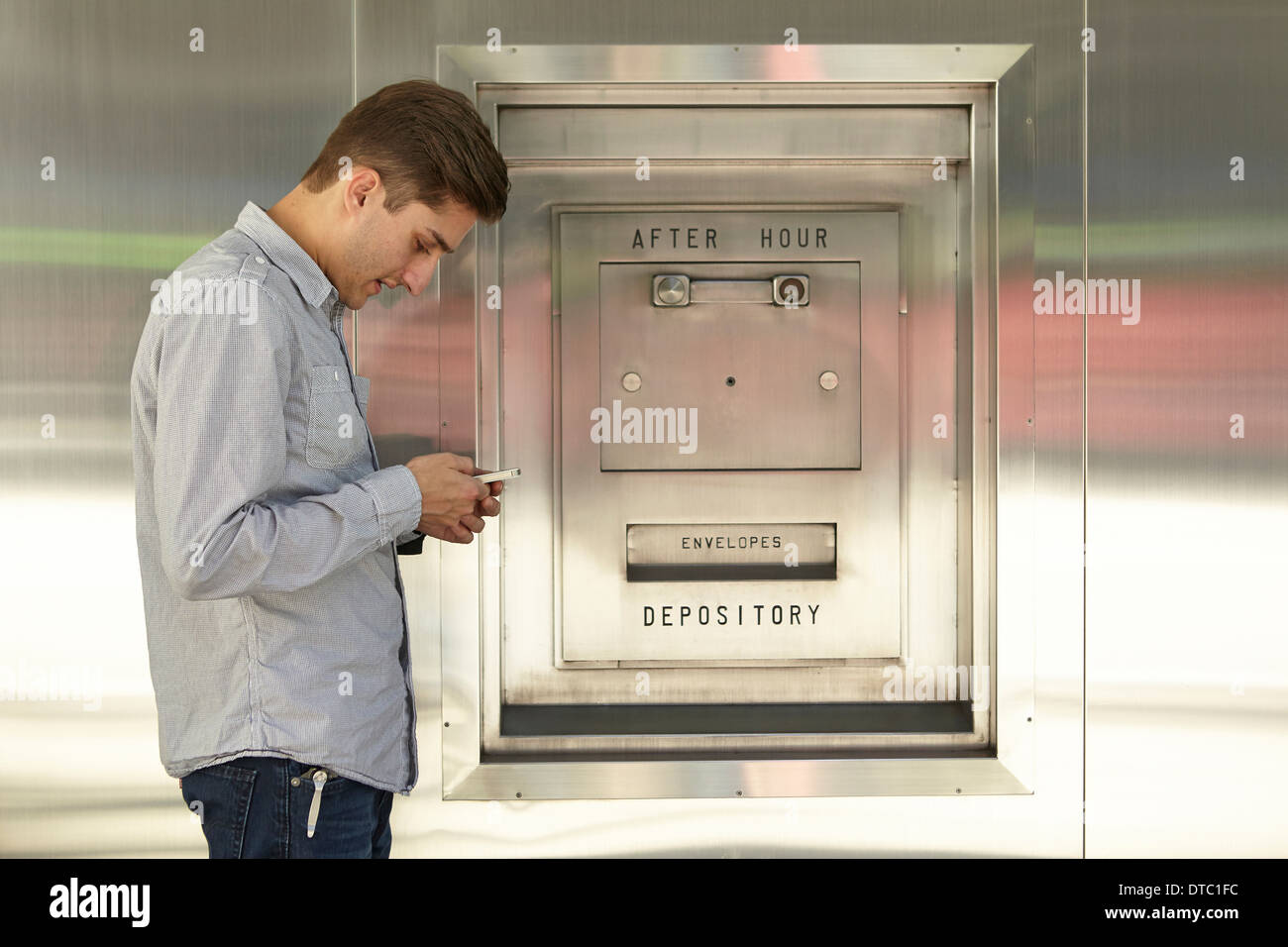 Hombre adulto medio en banca móvil junto al cuadro de depósito bancario Foto de stock