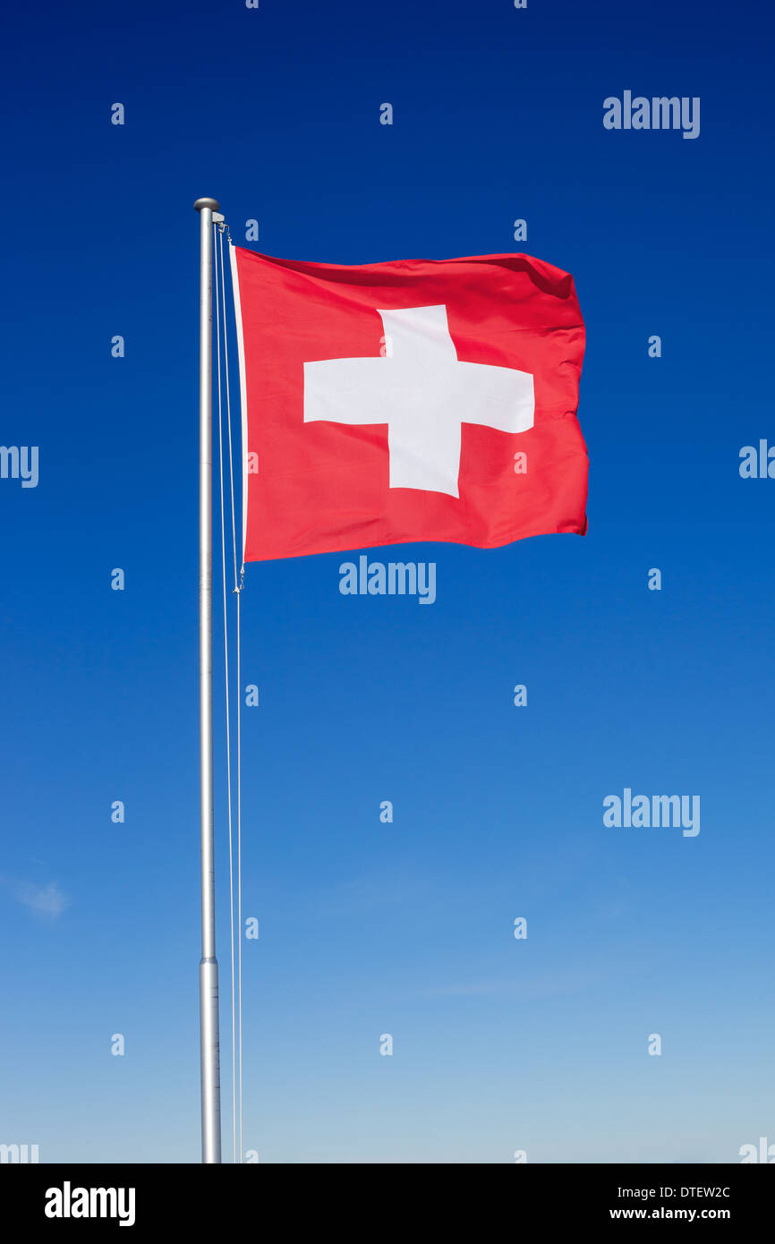 La bandera nacional de Suiza volando sobre un poste de metal contra un cielo azul claro. Foto de stock