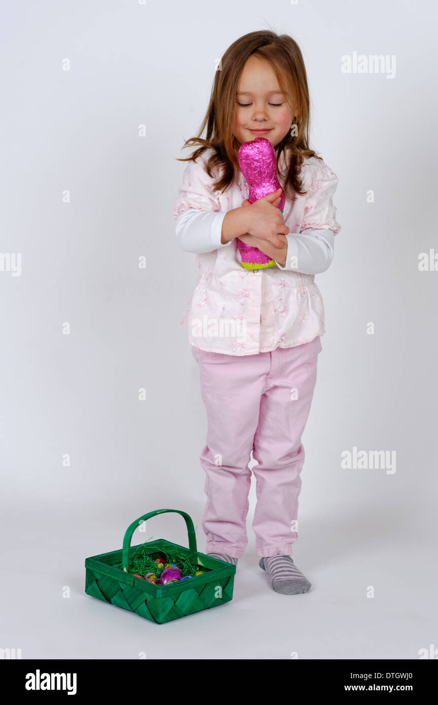 Una niña con una cesta de Pascua está abrazando un conejito de Pascua de chocolate Foto de stock