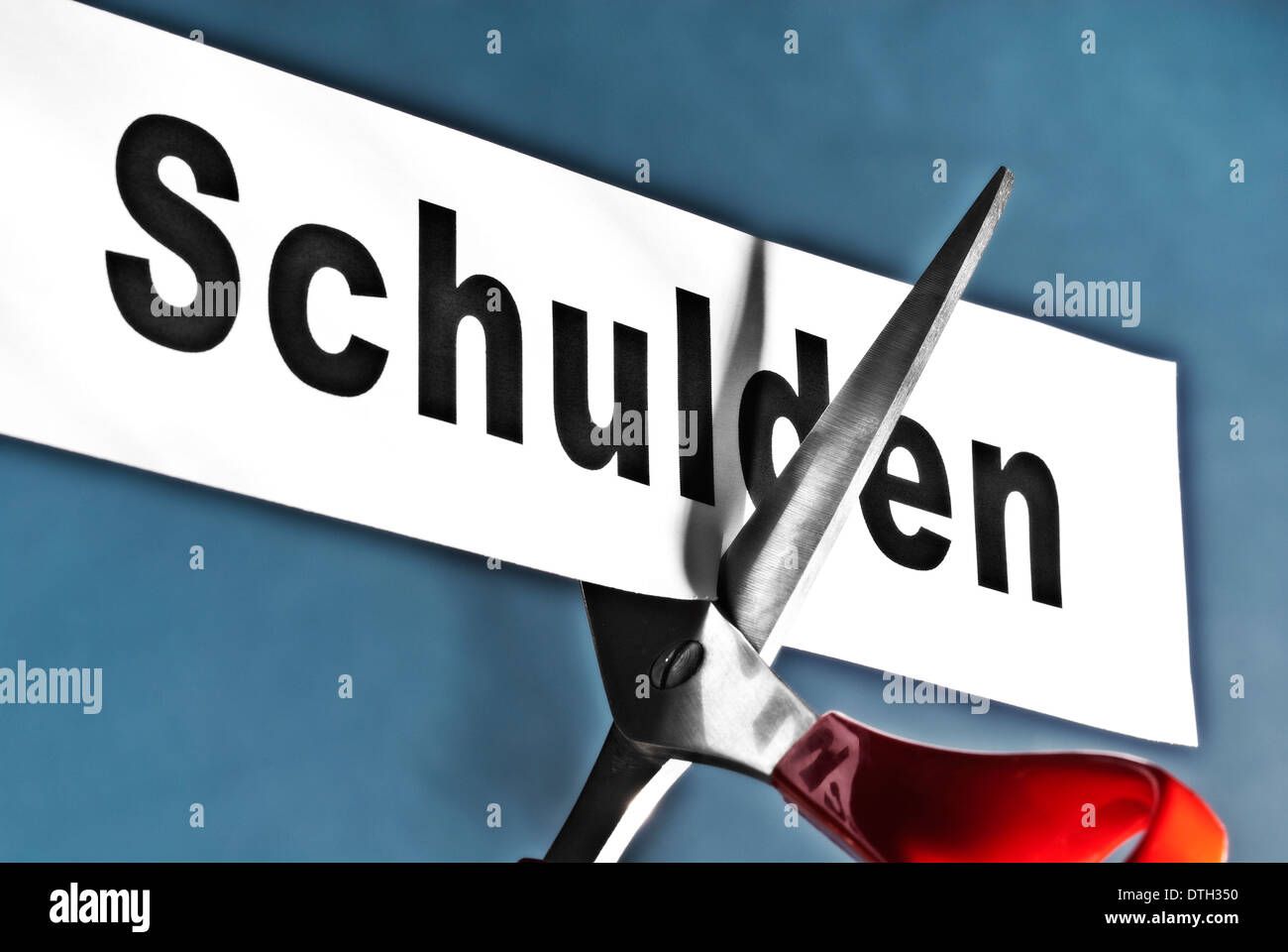 Tijeras corta un papel con la palabra 'Schulden' simbolizando un corte de pelo. Foto de stock