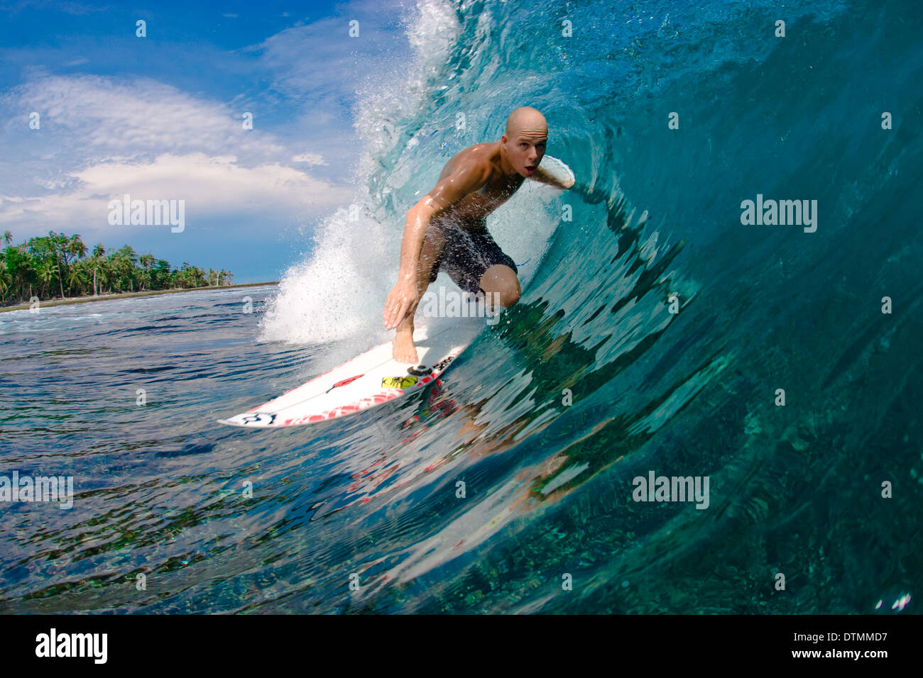 Surfer en una tabla de surf cabalgando una ola en el océano de agua de mar en la playa de onda voltear y haciendo trucos en un traje de neopreno y boardshorts Foto de stock