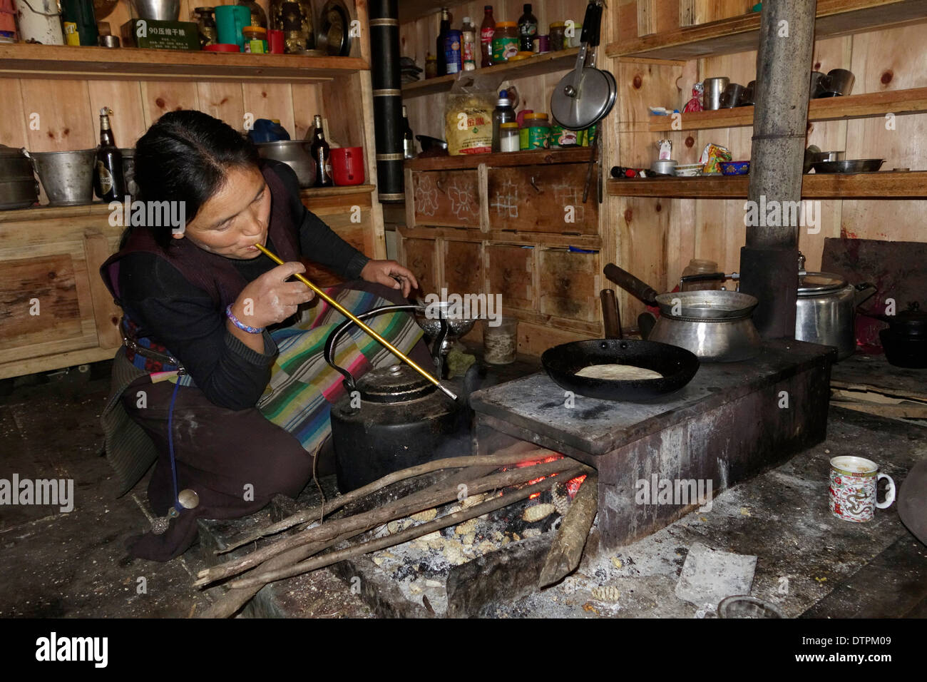 Mujer tibetana soplando a través de un poste de la tienda para avivar el fuego en una estufa de leña, Tsum Valle, Nepal. Foto de stock