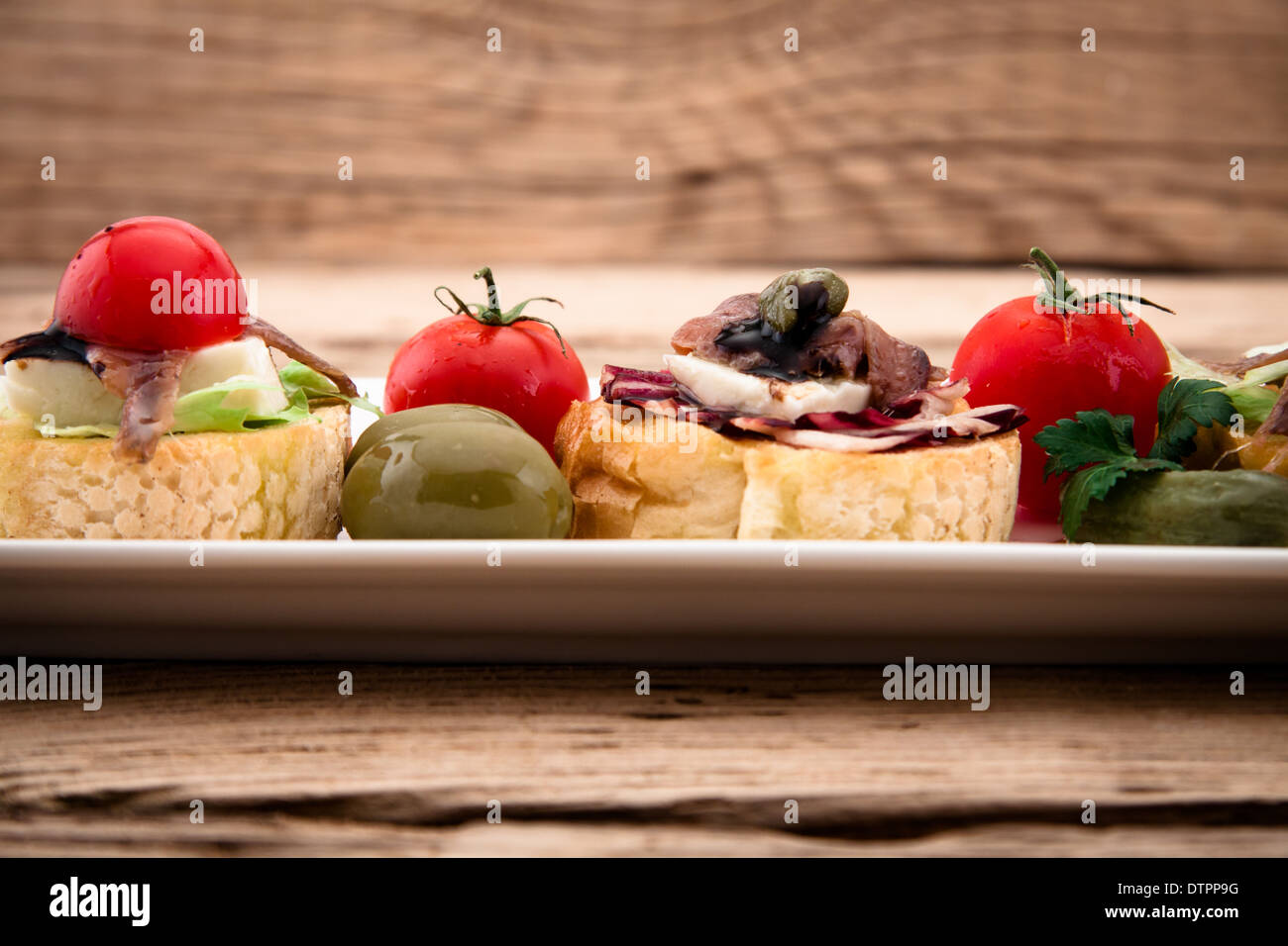 Crostini con queso mozzarella, tomate y anchoa en placa de madera Foto de stock