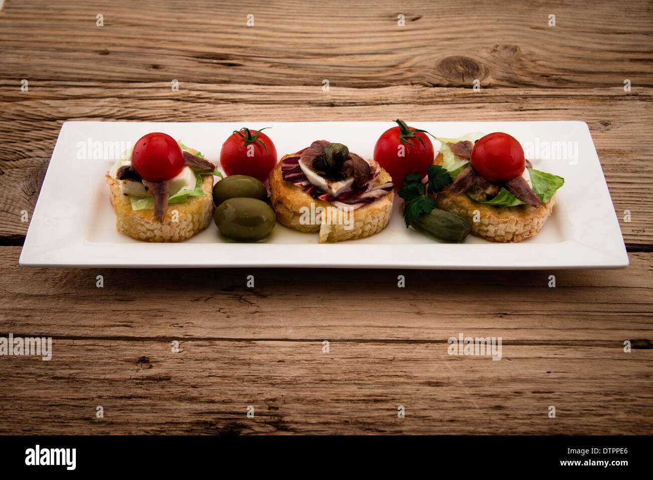 Crostini con queso mozzarella, tomate y anchoa en placa de madera Foto de stock