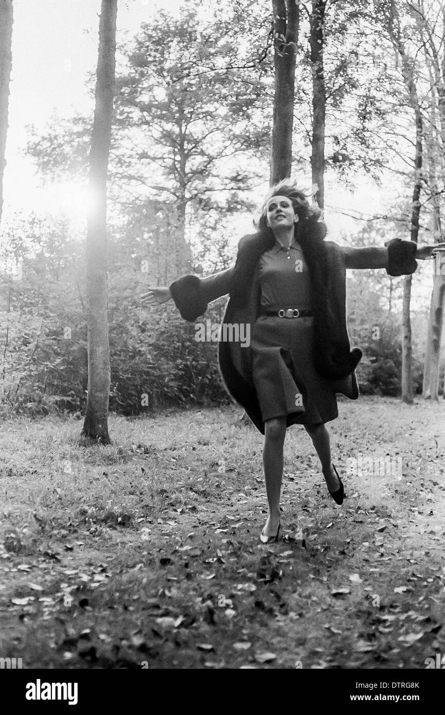 1960 modelo de pasarela con abrigo corriendo en el bosque Francia Europa Foto de stock