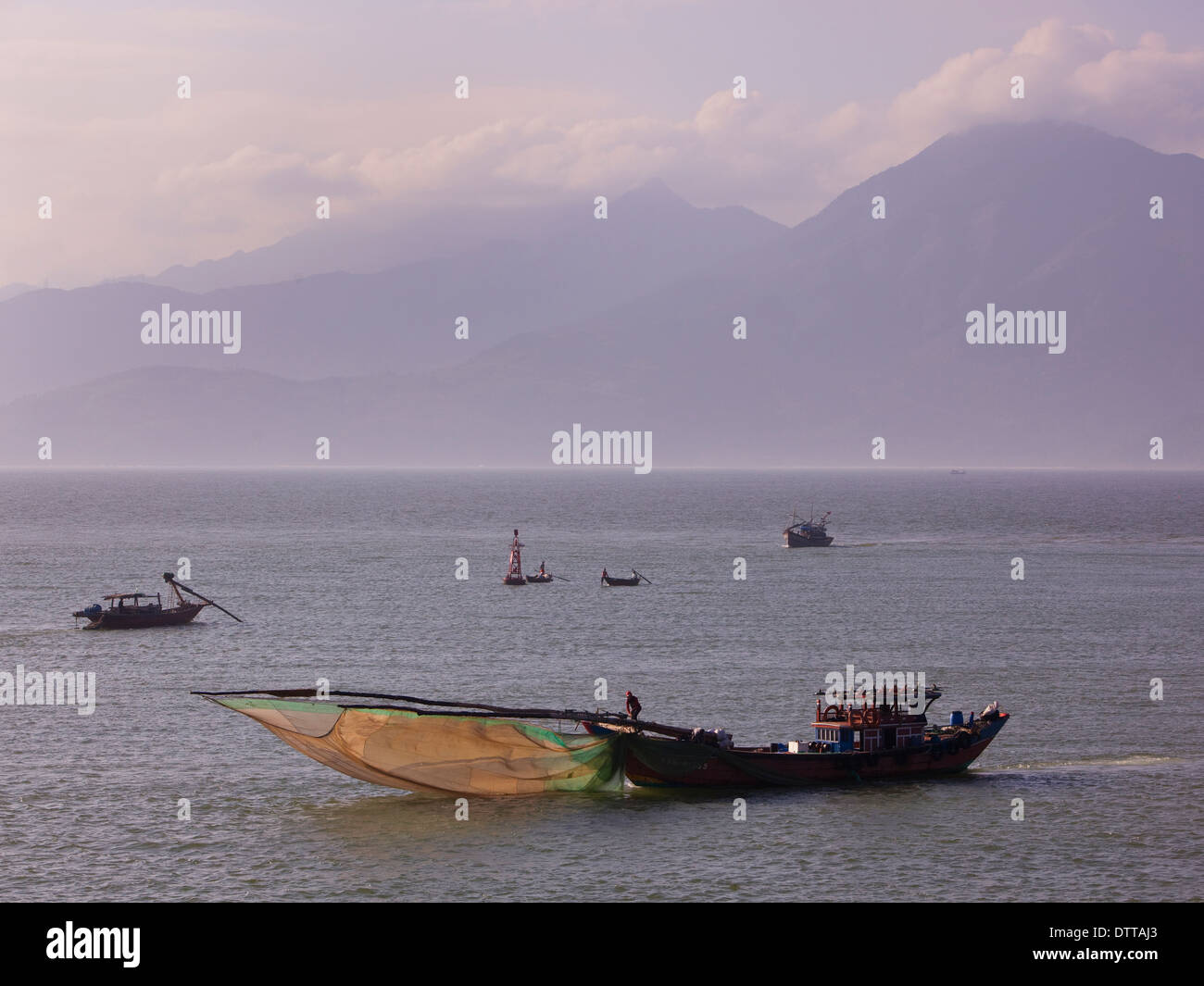Barcos de pesca que faenaban con arco amañadas scooping mosquiteros en Da Nang Bay con montañas como telón de fondo fuera de la ciudad de Da Nang, Vietnam Foto de stock
