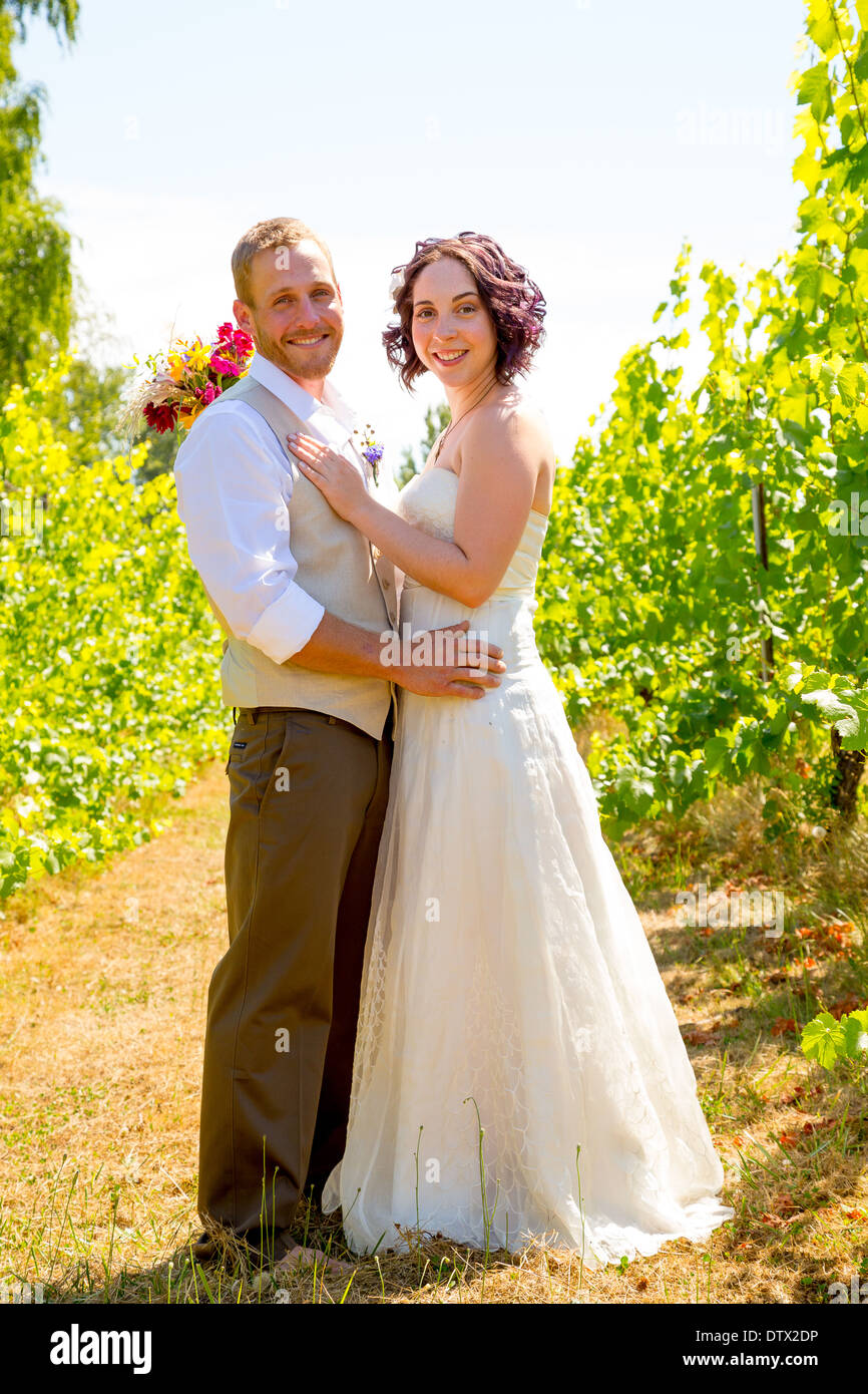 La novia y el novio juntos por un retrato en un viñedo en Oregon en el día de su boda. Foto de stock