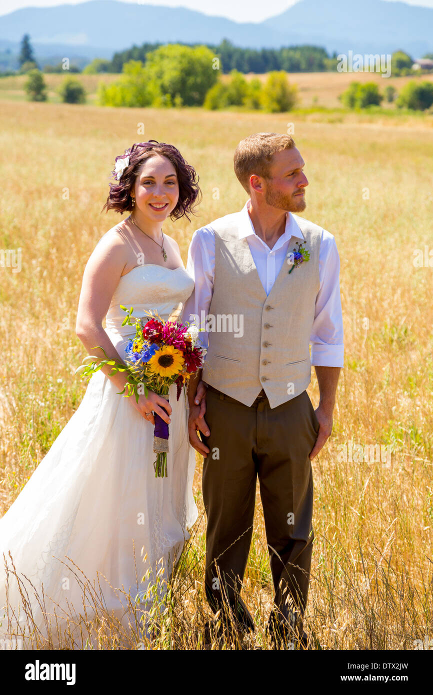 La novia y el novio juntos en el día de su boda por un campo en Oregon. Foto de stock