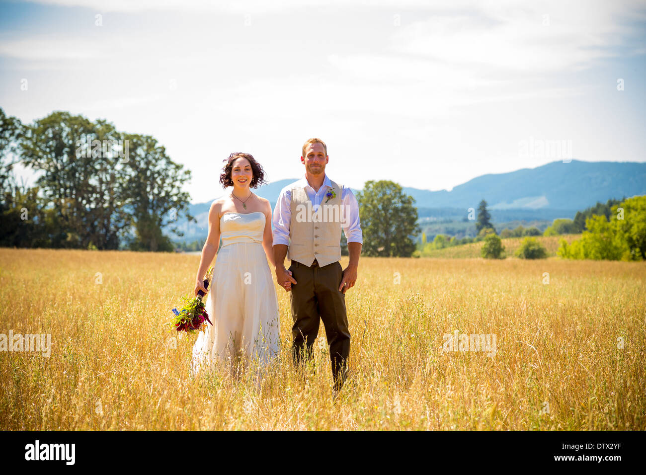 La novia y el novio de pie juntos en un campo en el día de su boda. Foto de stock