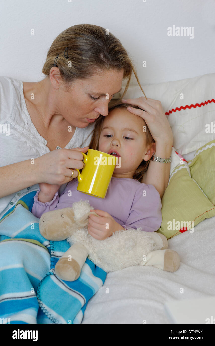 La madre de cuidar a su hija enferma, dispensación té caliente, niña acostada en la cama Foto de stock