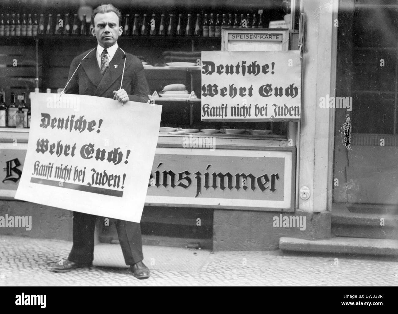 Un hombre, que lleva un cartel alrededor de su cuello leyendo '¡Alemanes! ¡Defendíos! ¡No pasen de los judíos!', se encuentra frente a una tienda judía, alrededor de las 1933. Este eslogan supuso un rico boicot a tiendas, médicos y abogados judíos, que comenzó el 01 de abril de 1933. La campaña antisemita fue organizada por el 'Comité Central para la Defensa de la Atrocidad Judía y la Agitación del Boicot'. Fotoarchiv für Zeitgeschichtee / NO WIRE SERVICE Foto de stock