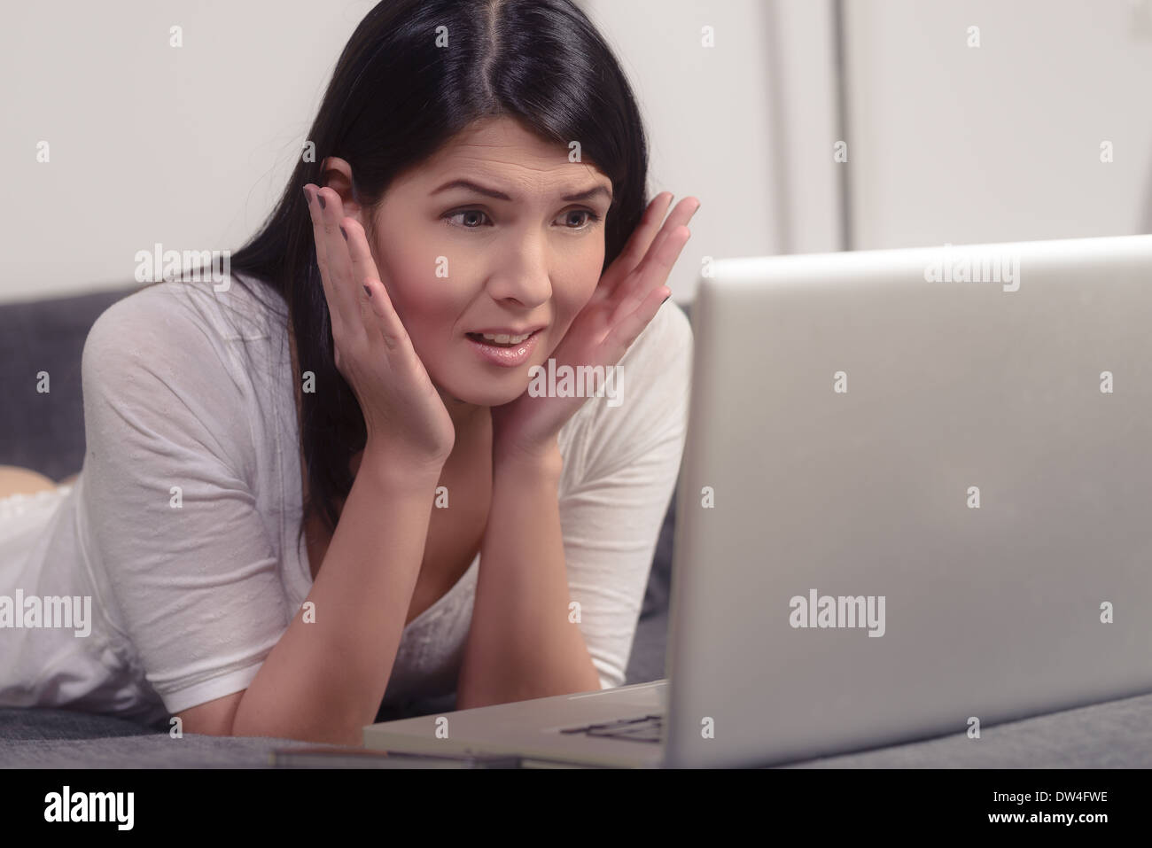 Joven morenita mujer mirando su ordenador portátil con una expresión horrorizada Foto de stock