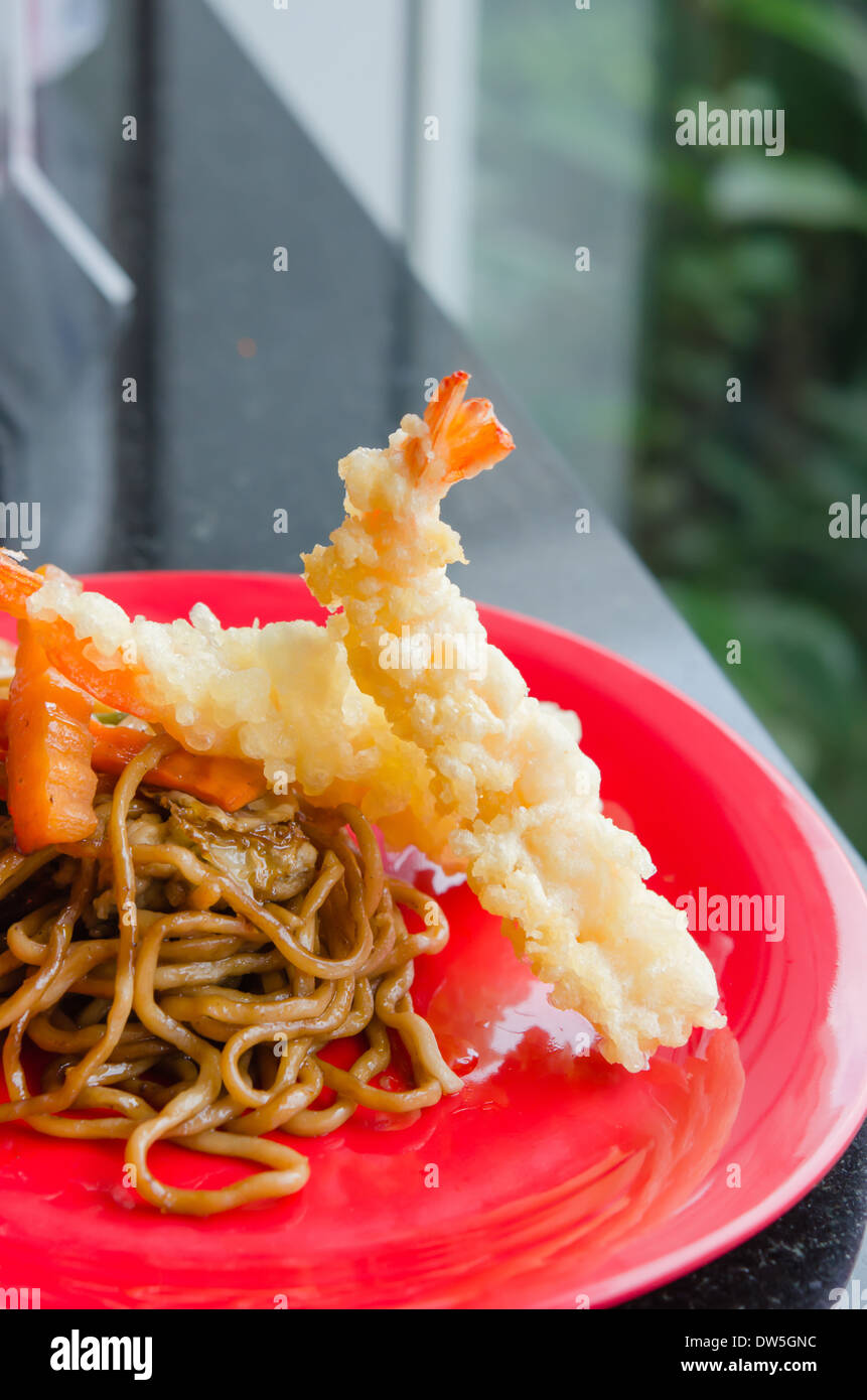 Fideos fritos con verduras y gambas fritas en plato rojo Foto de stock