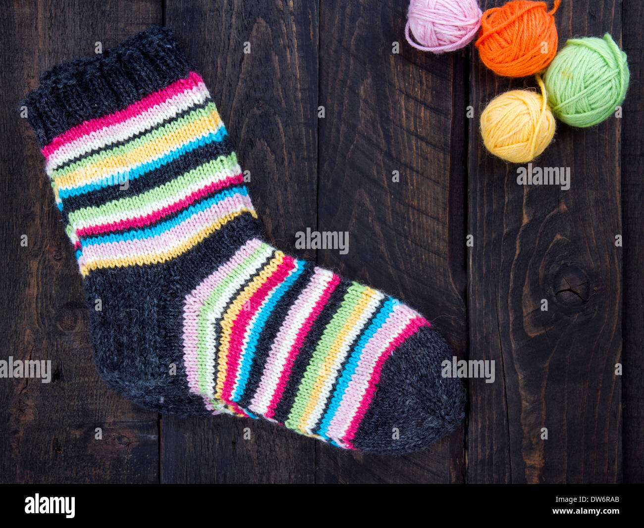 Par de calcetines de lana a rayas multicolor sobre fondo vintage de madera oscura con pelotas multicolores de hilo y habitación para copiar el espacio Foto de stock