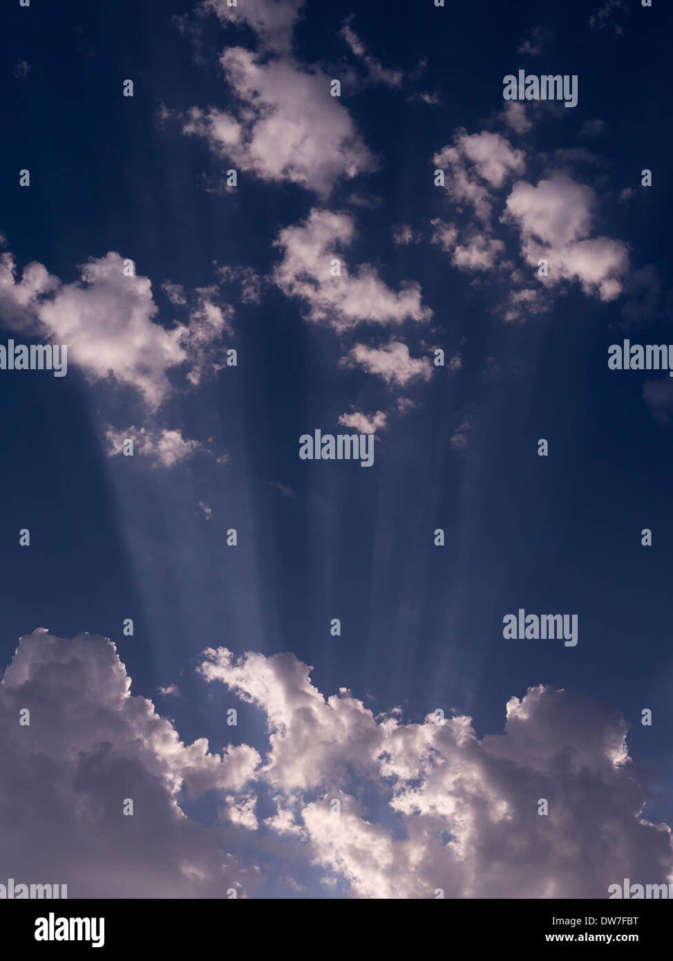 Irradiando rayos de sol y nubes blancas contra el cielo azul Foto de stock