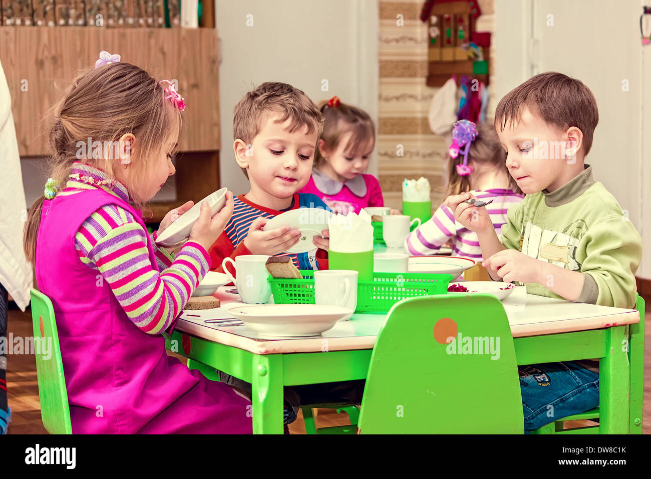Los niños y niñas del grupo de niños sentados a la mesa con la comida y comer apetitoso Foto de stock