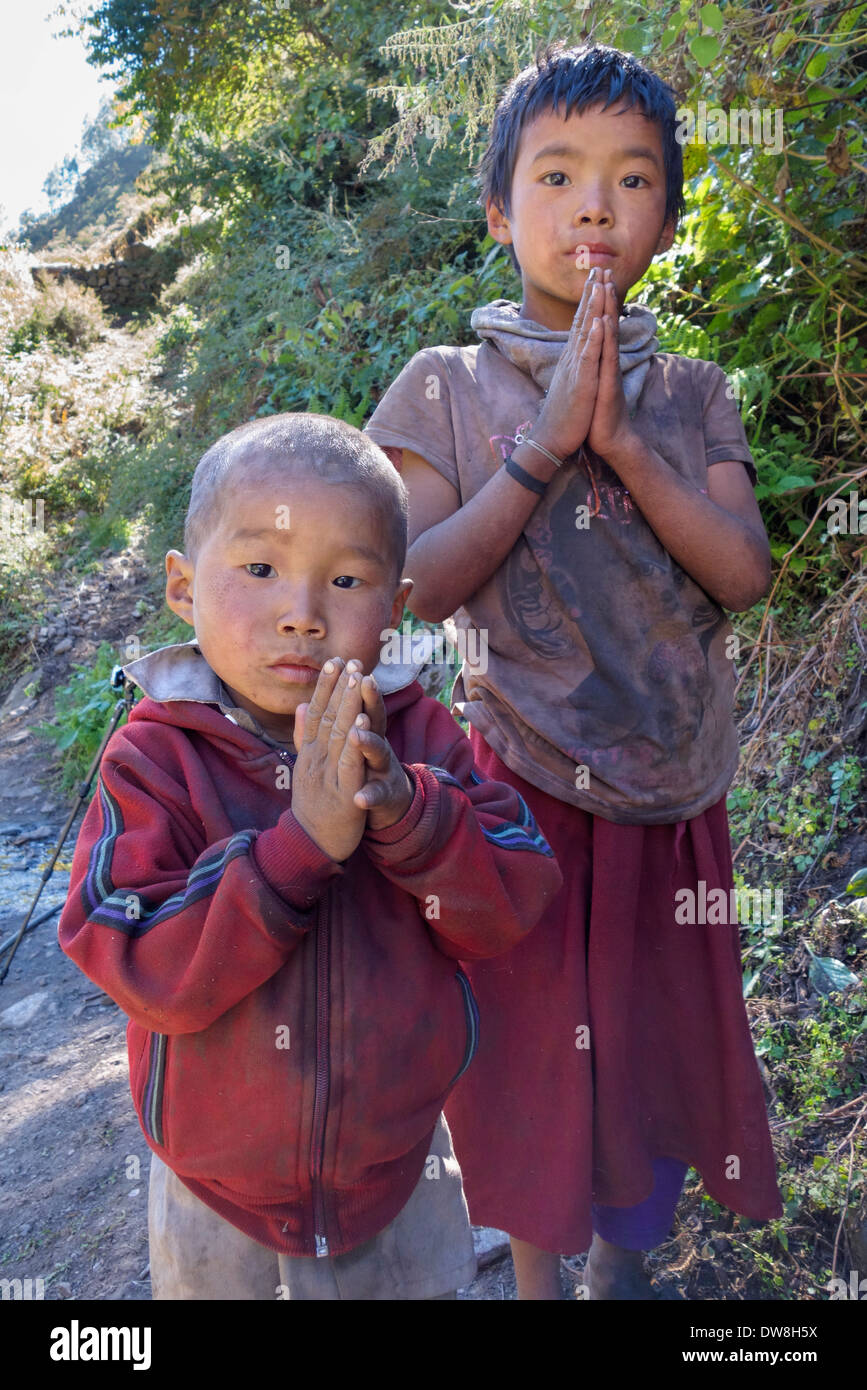 Los niños nepaleses sosteniendo sus manos juntas en el gesto namaste a lo largo de un sendero en el Manaslu región de Nepal. Foto de stock