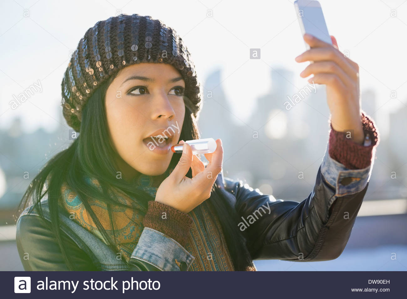 Mujer con teléfono inteligente para aplicar lápiz de labios afuera Foto de stock