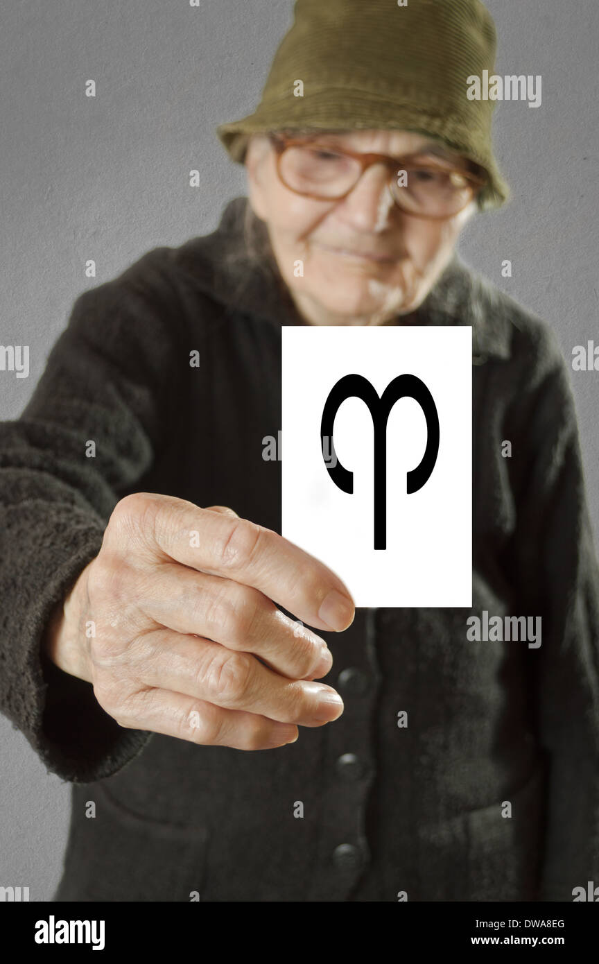 Anciana sujetando la tarjeta impresa con horóscopo signo de Aries. El enfoque selectivo en la tarjeta y los dedos. Foto de stock