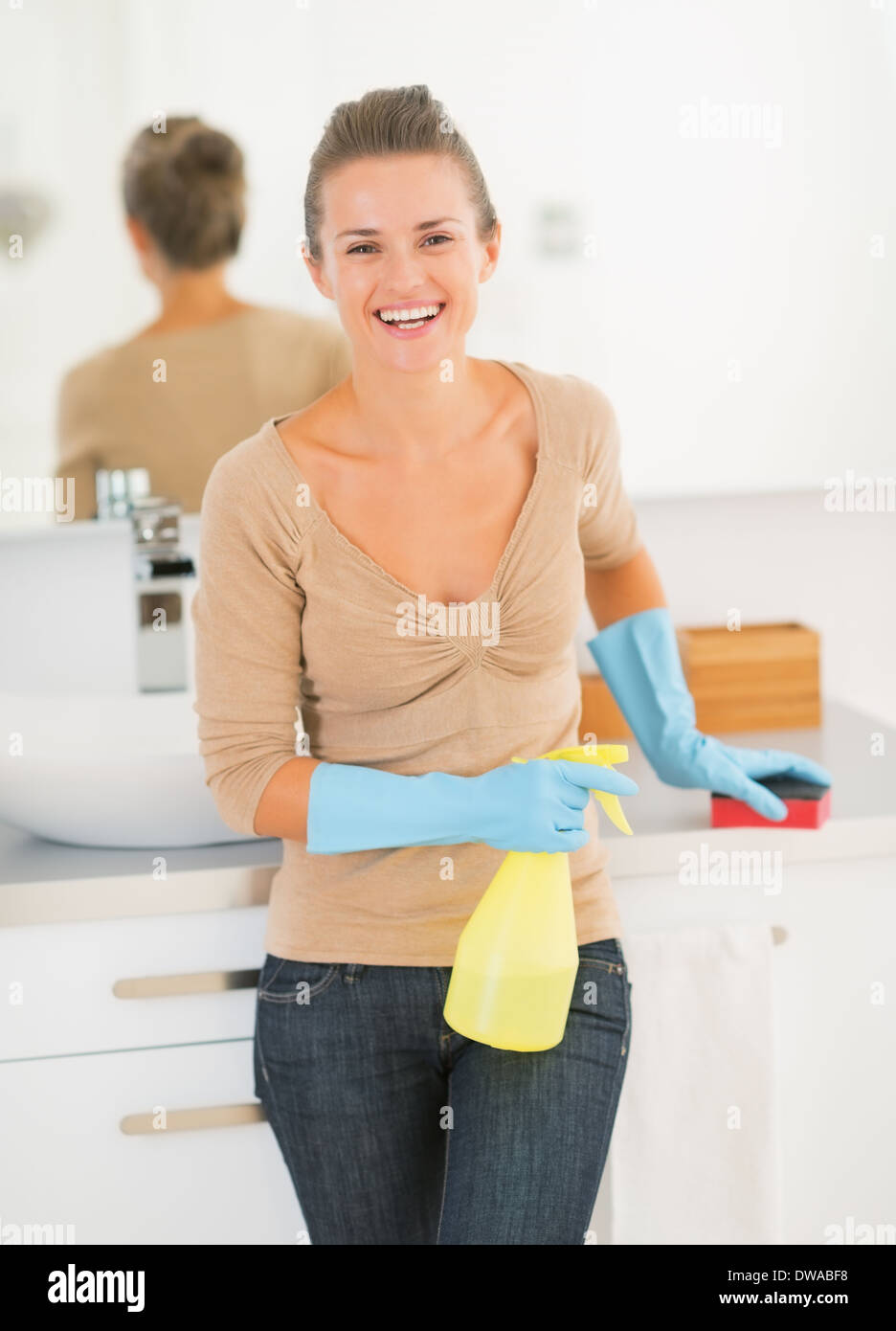 Retrato de ama de casa feliz con atomizador y la esponja en el baño. Foto de stock