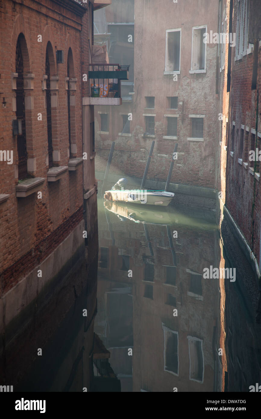 Rayos de sol que brilla sobre un barco en un pequeño canal lateral con edificios antiguos Venecia Italia Foto de stock