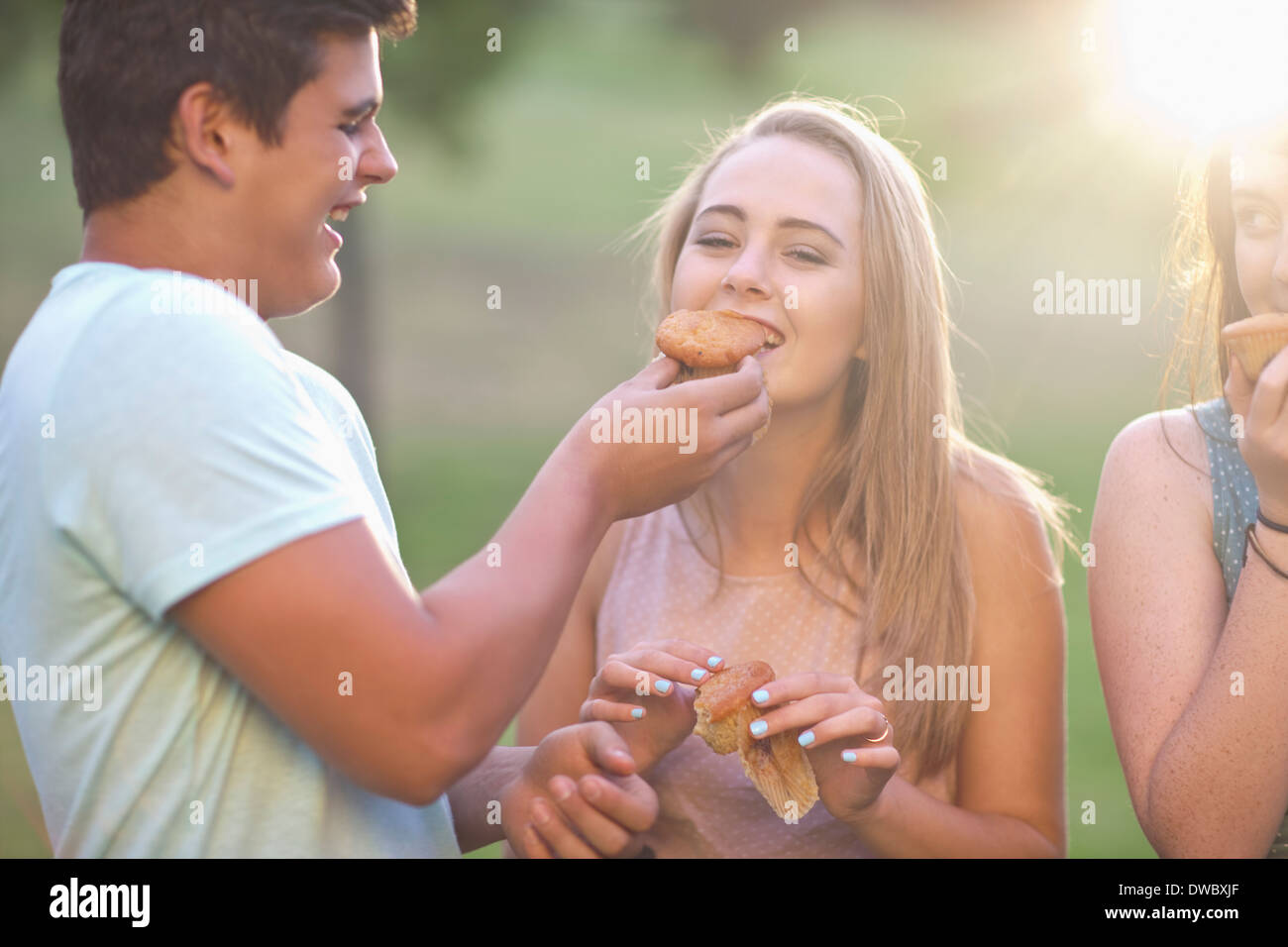 Alimentación chico chica, amigo en segundo plano. Foto de stock