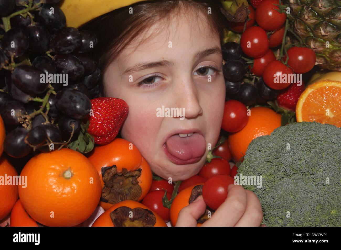 Los jóvenes caucásicos cara de la niña rodeada de frutales y hortalizas no disfrutar comiendo healthly , cinco al día, Inglaterra, Reino Unido. Foto de stock