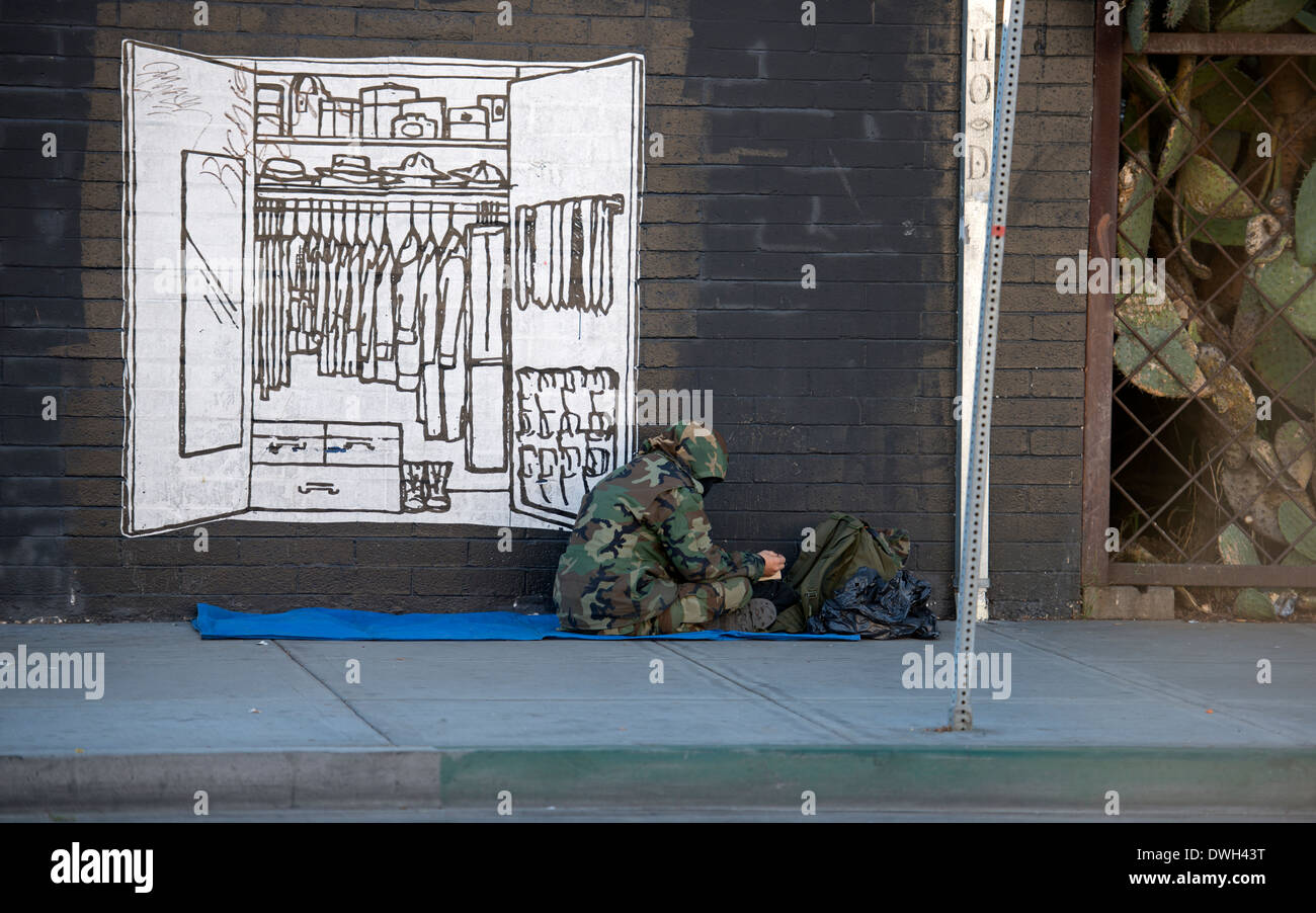 Personas sin hogar hombre sentado en la acera junto al mural del armario para ropa, East Village, San Diego, California Foto de stock
