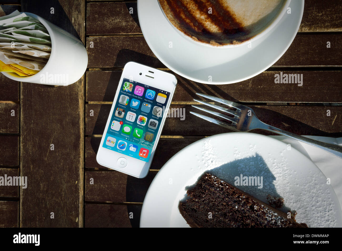 IPhone 4s sobre la mesa con el pastel y el Cappuccino Foto de stock