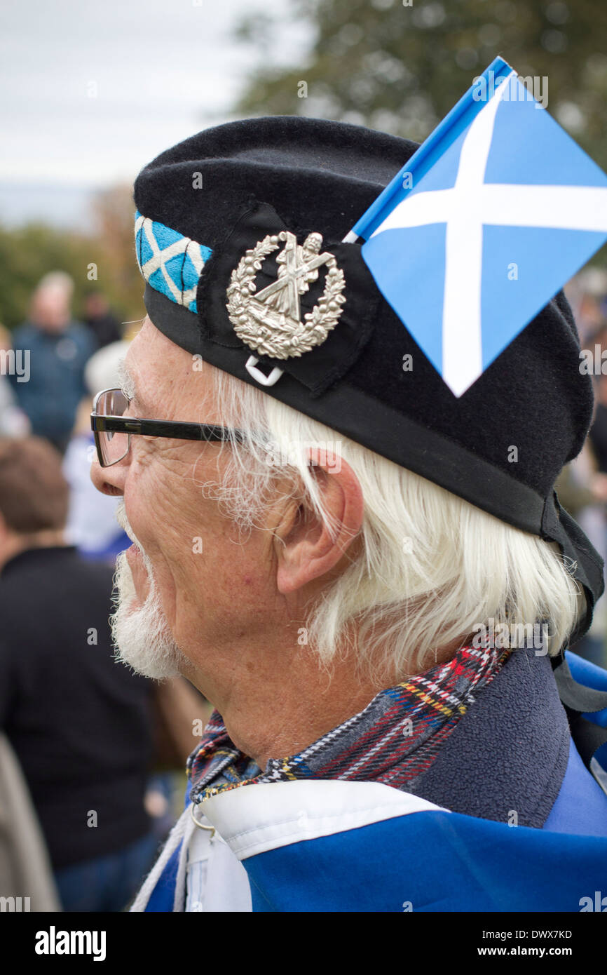 Un hombre con una pequeña bandera saltire escocés y una gorra militar escuchando en Edimburgo, durante un mitin pro-independencia en Edimburgo Foto de stock